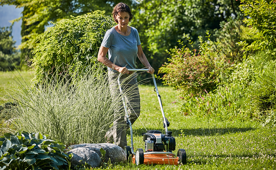 Une femme tondant la pelouse dans un jardin d’été à l’aide d’une tondeuse mulching STIHL RM 2 R