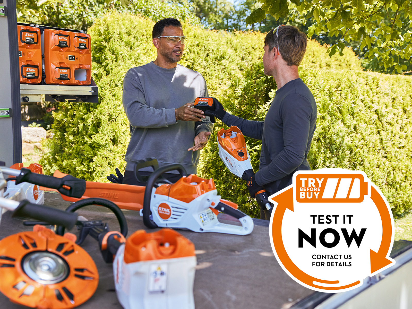 Deux hommes insérant une AP 300 S dans un taille-haies à batterie. Autocollant « Try before Buy » avec l’invitation « Test it Now – contact us for details »