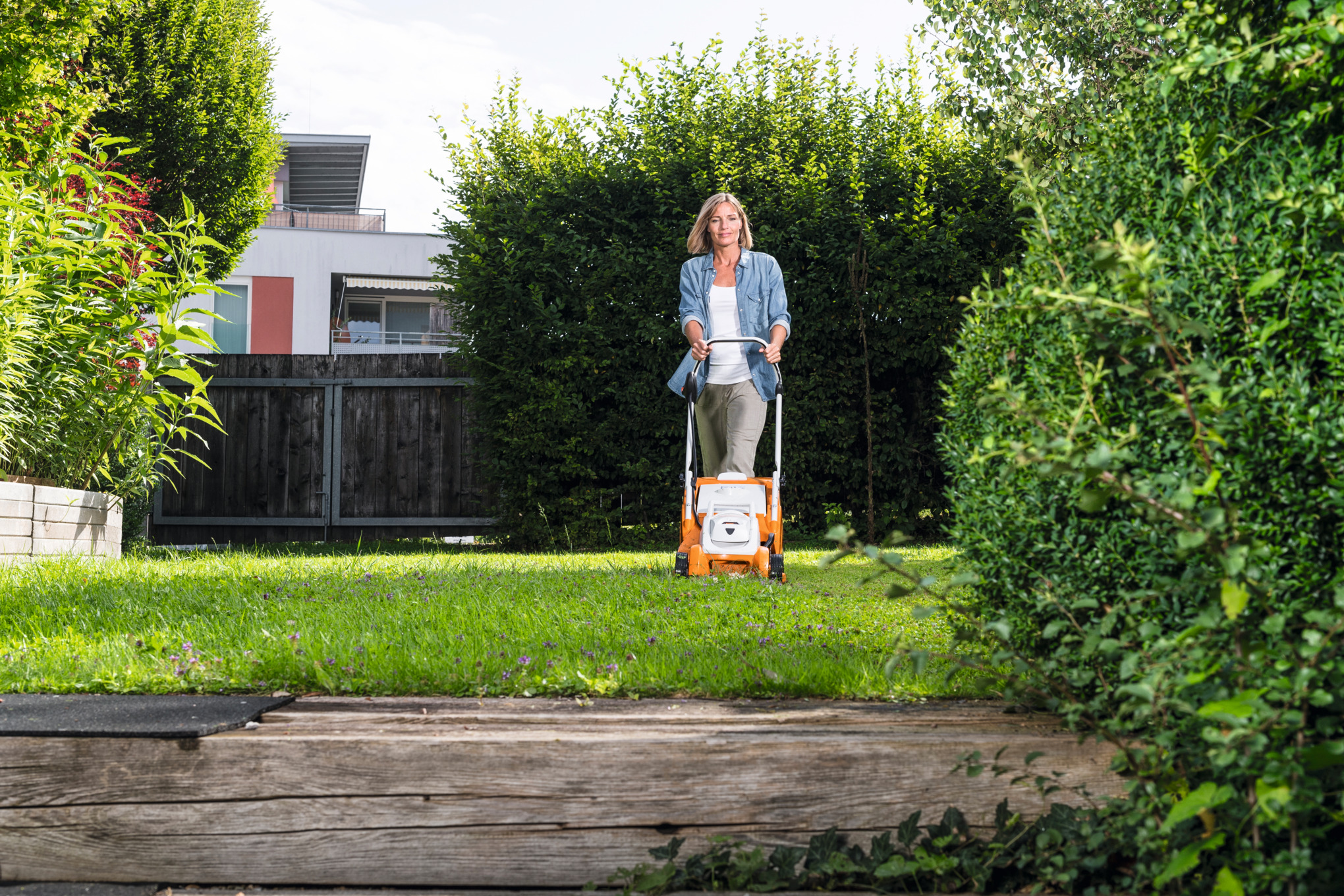Une femme tond la pelouse de son jardin avec une tondeuse à gazon sans fil STIHL RMA 339