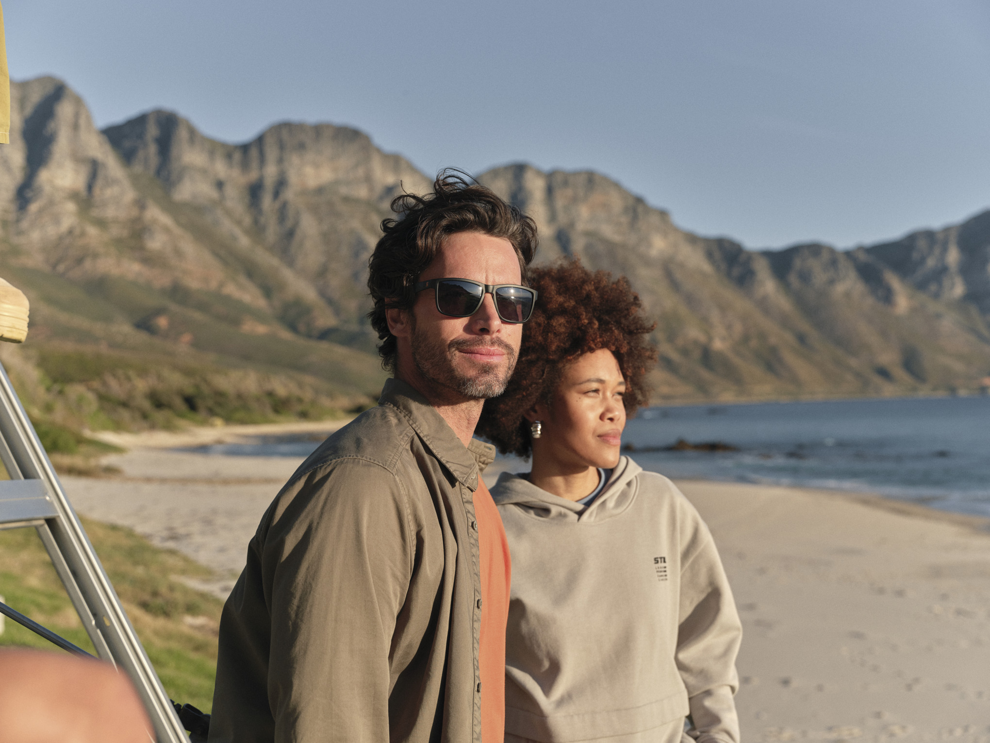 Un homme et une femme à la plage portent des vêtements de la collection STIHL Fan Kogel Bay, et regardent vers la mer