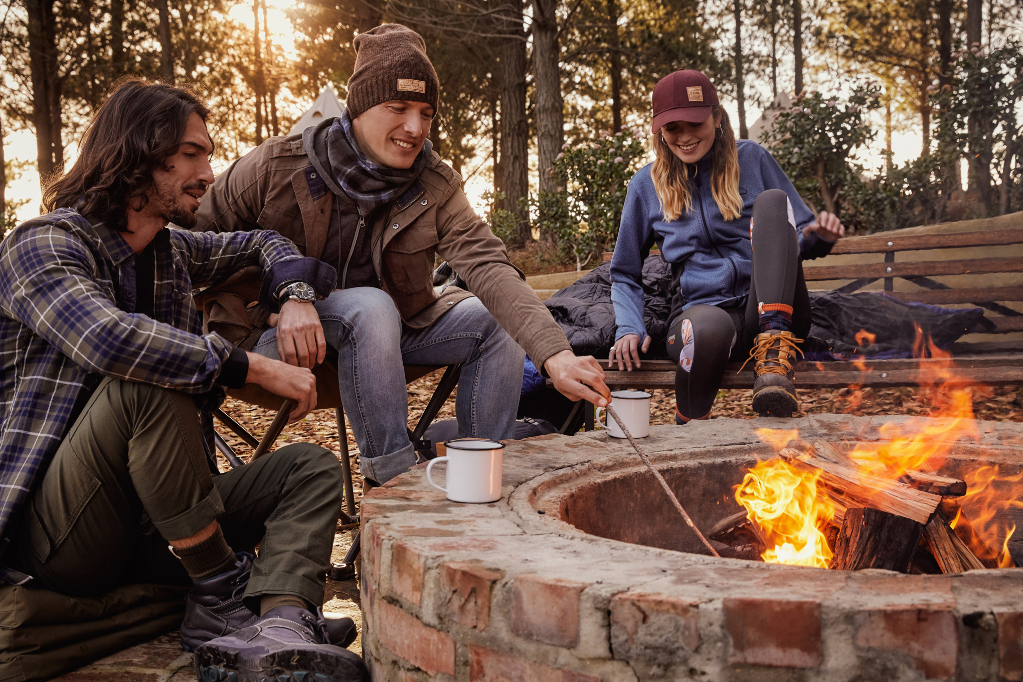 2 hommes et une femmes sont assis autour d'un feu de camp et portent des vêtements de la collection officielle STIHLnts de la co