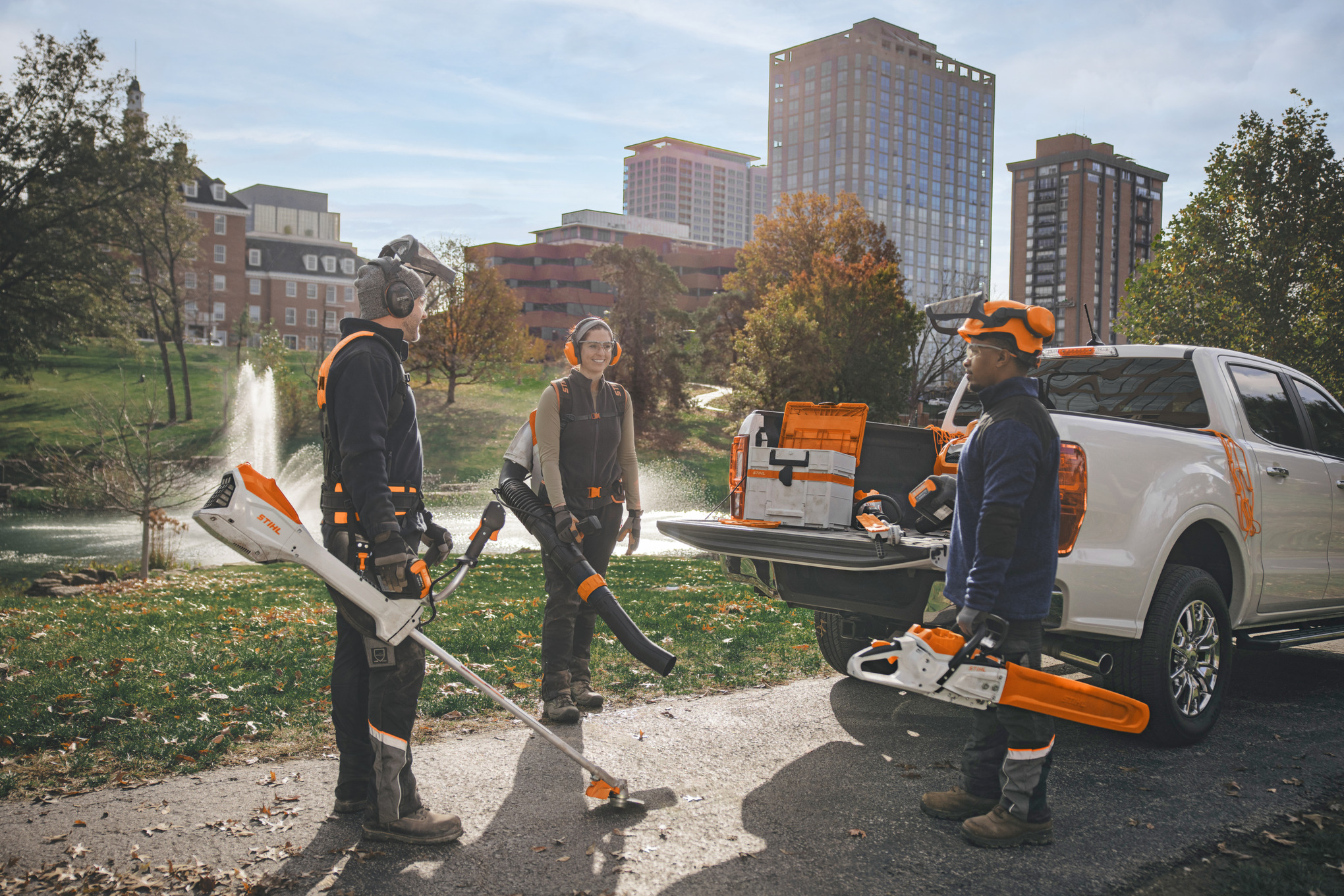 Un groupe de paysagistes professionnels, rassemblés autour de leurs véhicules, se préparent à travailler avec des outils électriques à batterie STIHL. 