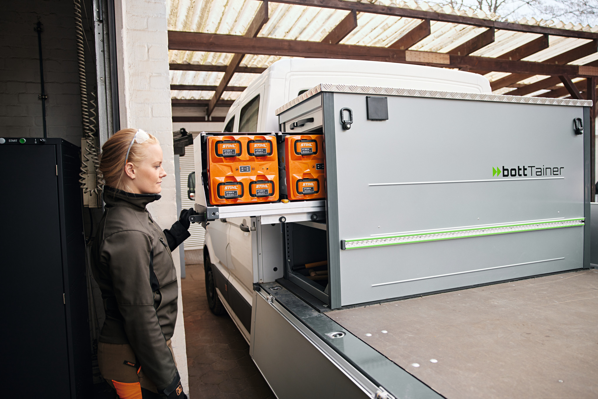 Femme à côté d’un véhicule avec plateau de chargement en train de manipuler les batteries dans le bottTainer