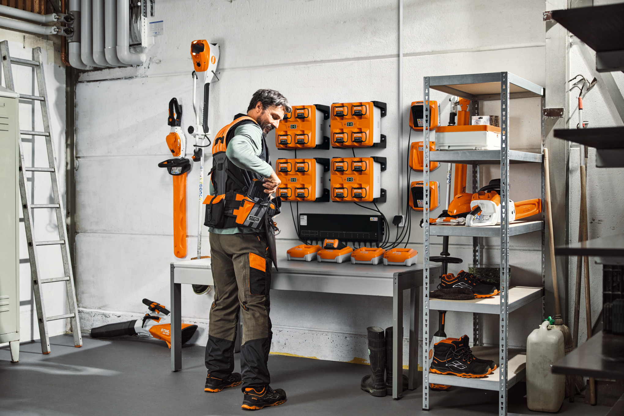 Un homme dans un entrepôt avec des outils et des batteries STIHL porte le système de harnais modulaire STIHL ADVANCE X-Flex. 