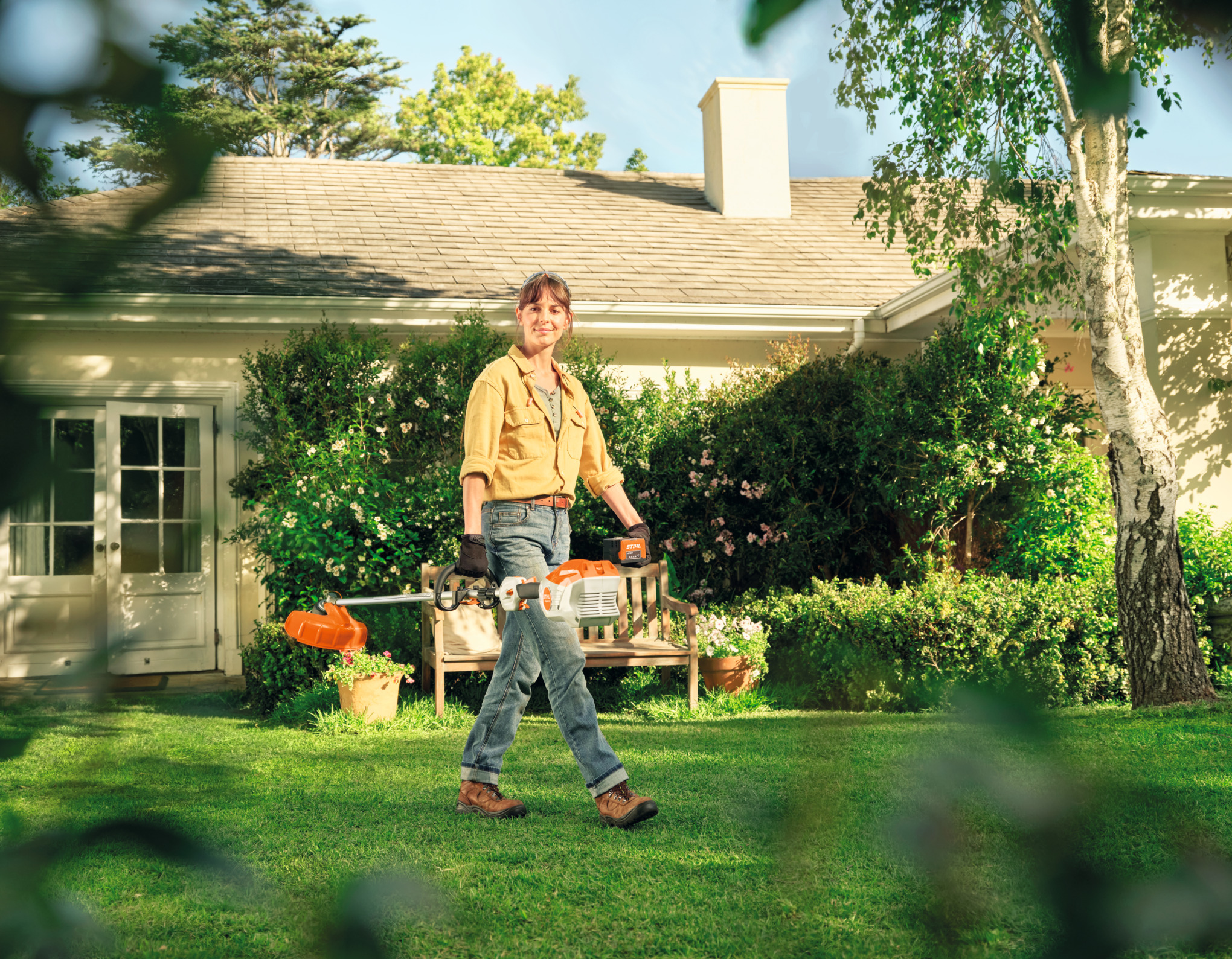 Une femme traverse son jardin avec une débroussailleuse à batterrei FSA 80 R à la main