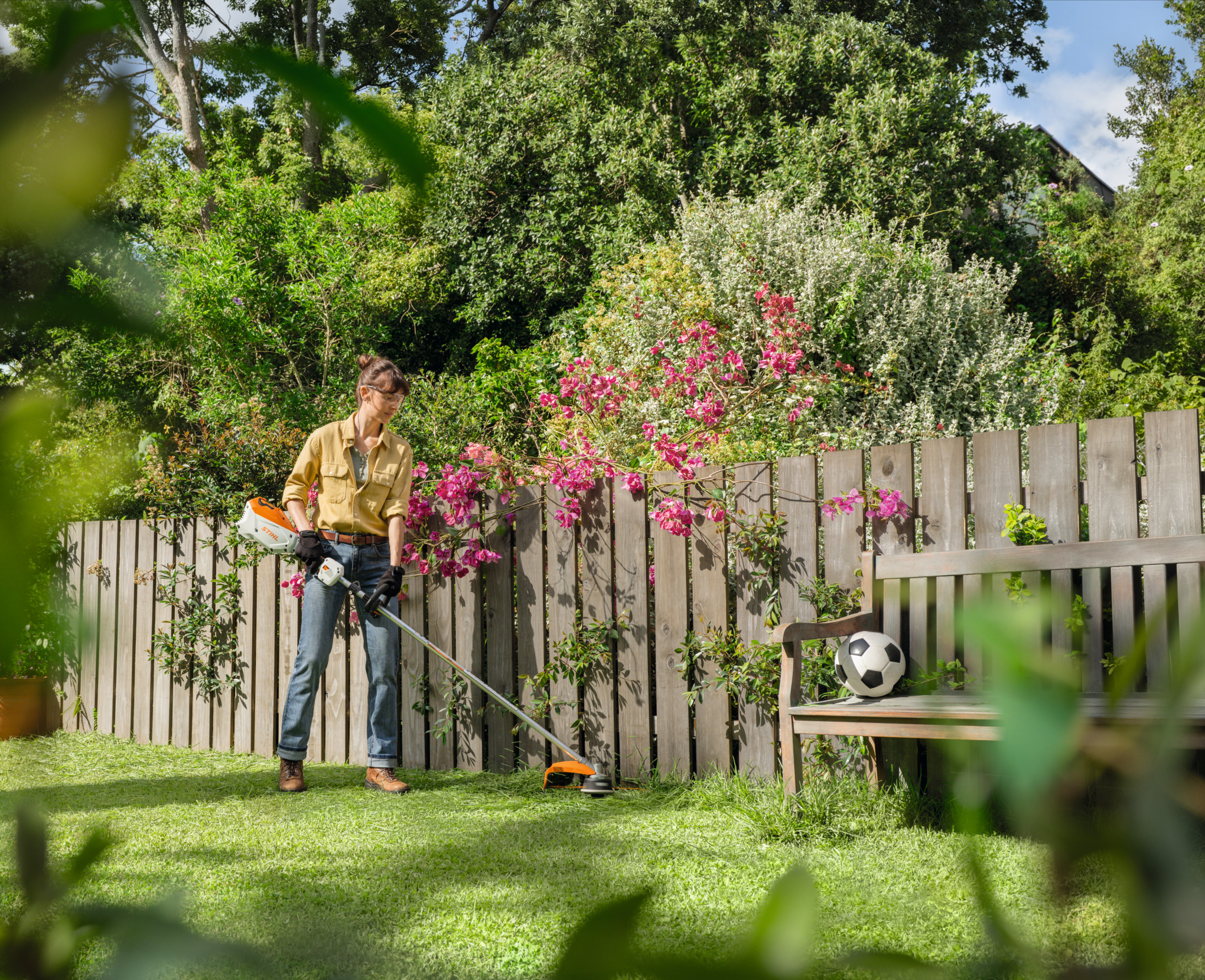  Une femme traverse son jardin avec une débroussailleuse FSA 80 R à la main