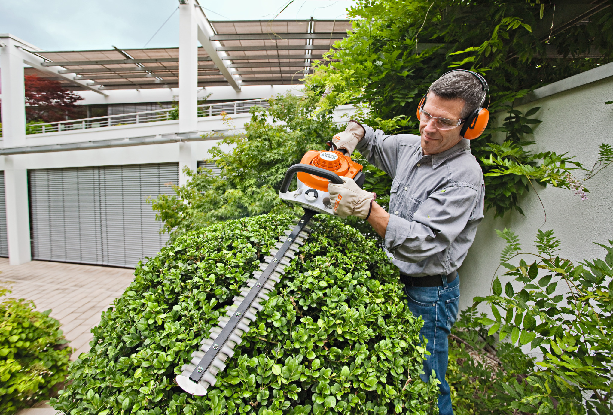 Un homme taille la haie de son jardin avec un HS 46