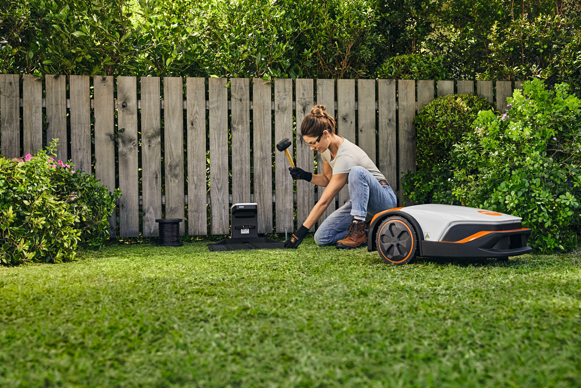 Femme dans un jardin, un marteau à la main, installant la station d’accueil iMOW®