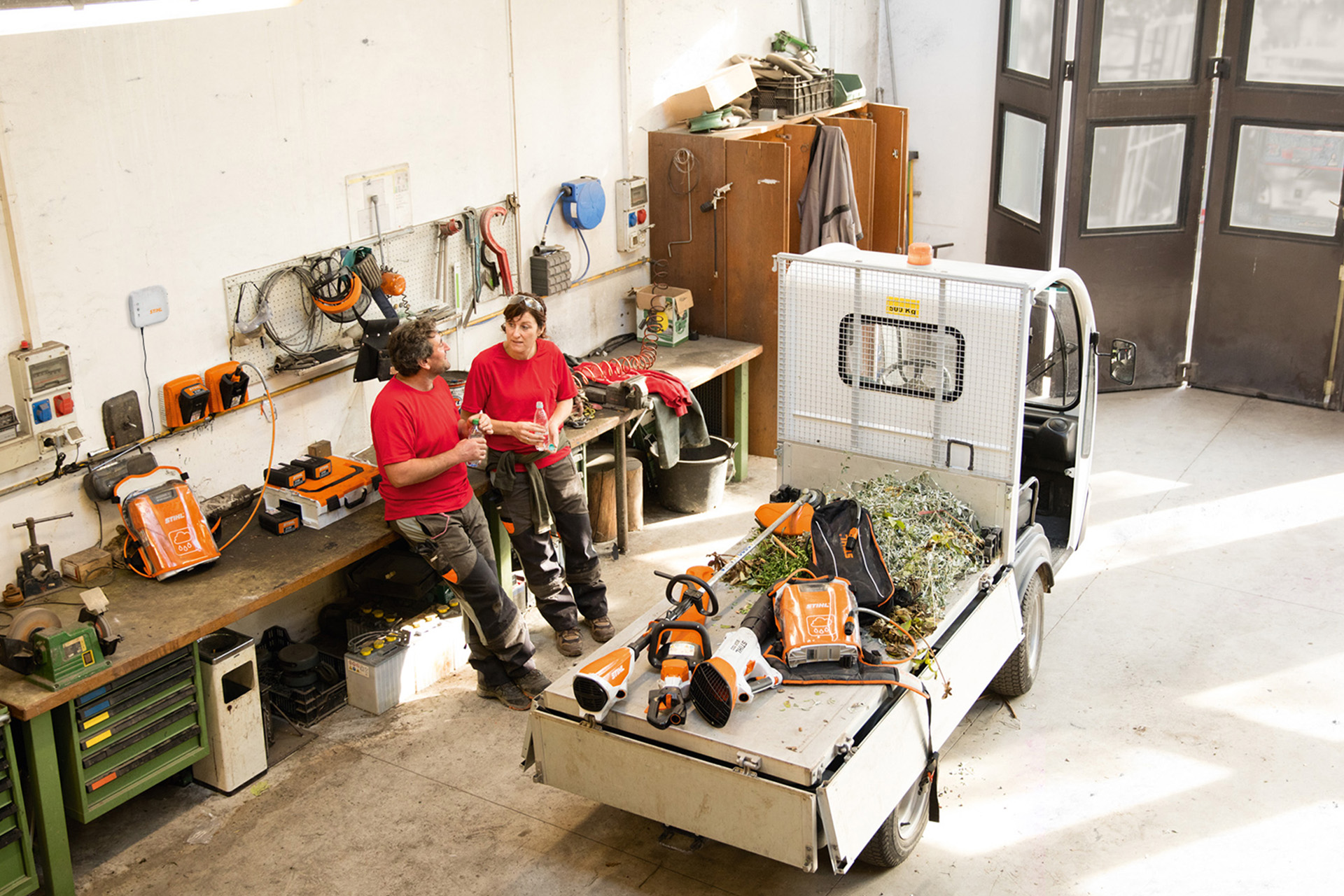 Deux personnes dans un atelier font une pause à côté d’un petit camion avec des outils STIHL sur la plateforme de chargement