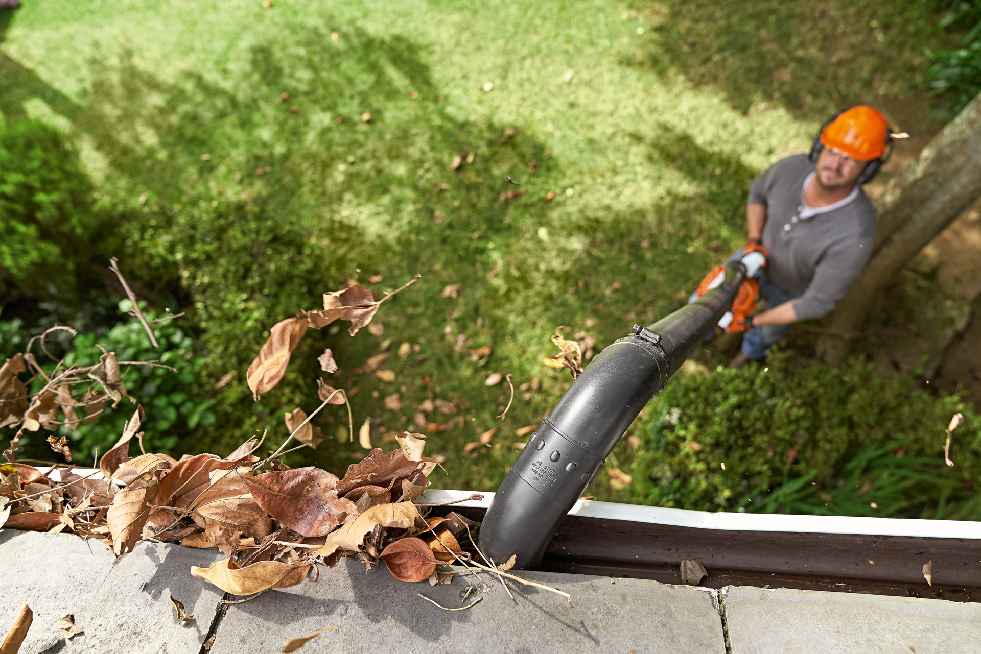 Vue aérienne d’une gouttière remplie de feuilles nettoyée par un homme au sol avec un souffleur de feuilles STIHL équipé d’un kit de nettoyage de gouttières