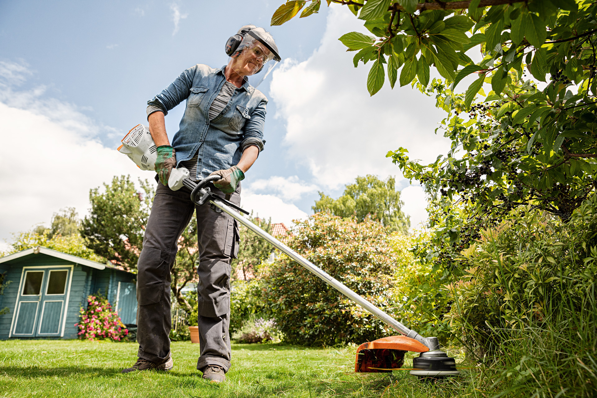 Femme portant une protection faciale et auditive utilisant un coupe-bordures thermique STIHL FS 56 R dans un jardin.