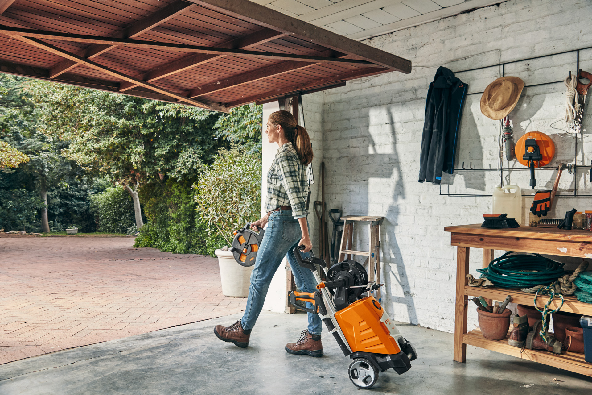 Une femme sortant d’un garage avec le nettoyeur haute pression STIHL RE 130 PLUS en vue de son utilisation