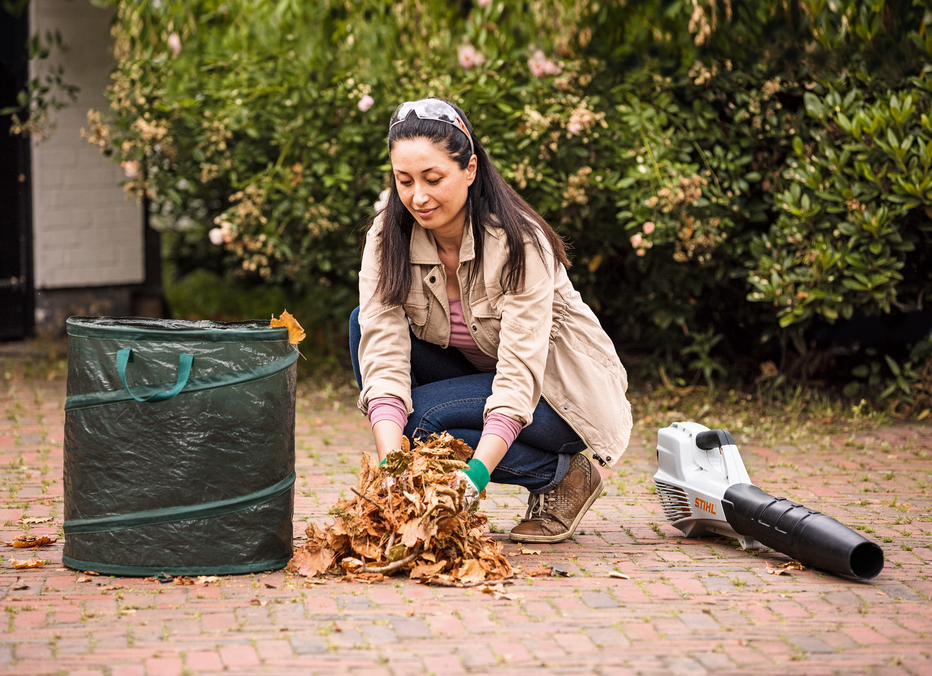 Une femme, à côté d’un souffleur de feuilles STIHL BGA 57 posé au sol, met des feuilles dans un sac à déchets végétaux