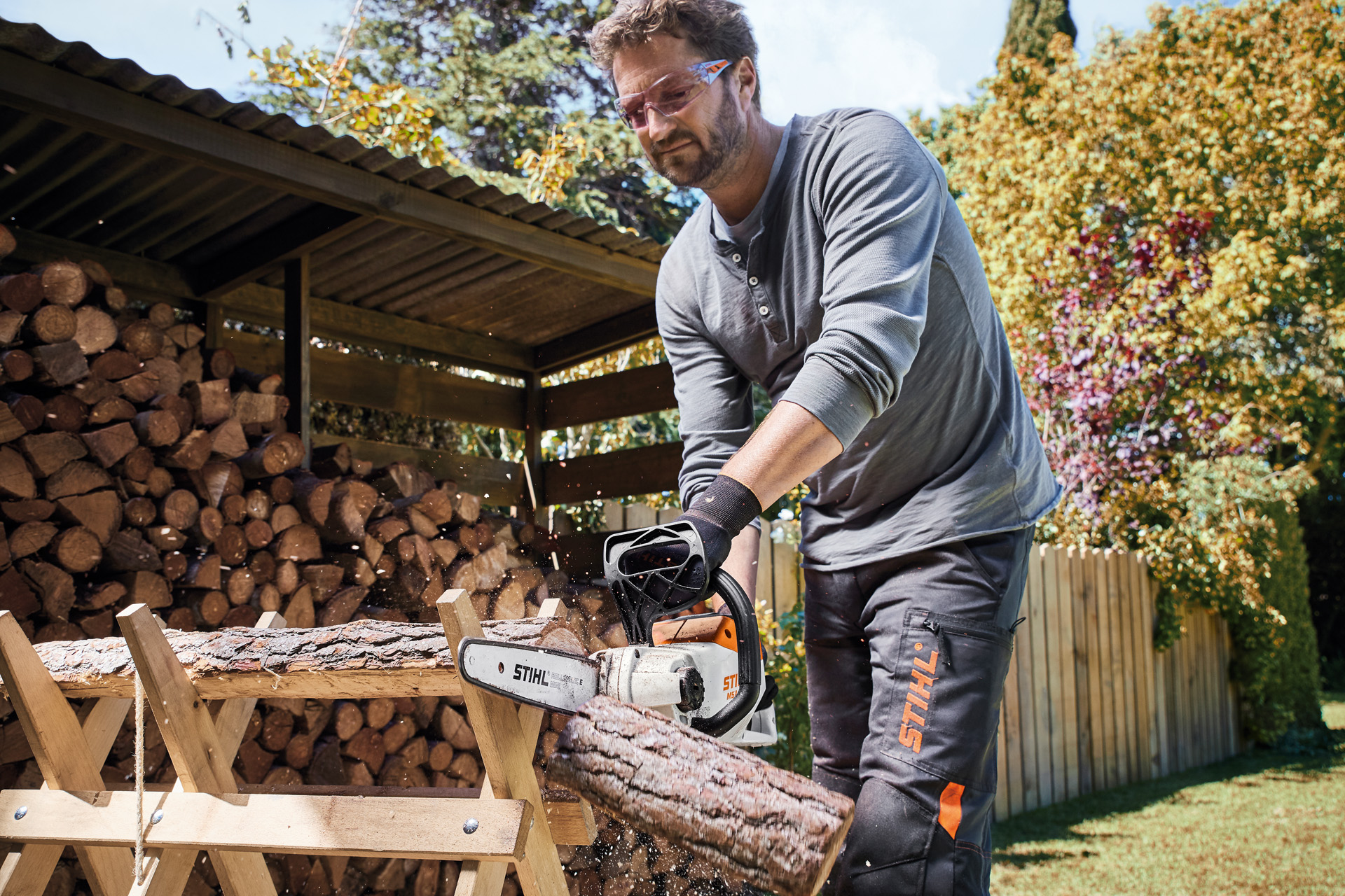 Homme portant des lunettes de protection en train de scier une bûche avec une tronçonneuse à batterie STIHL MSA 140 C-B
