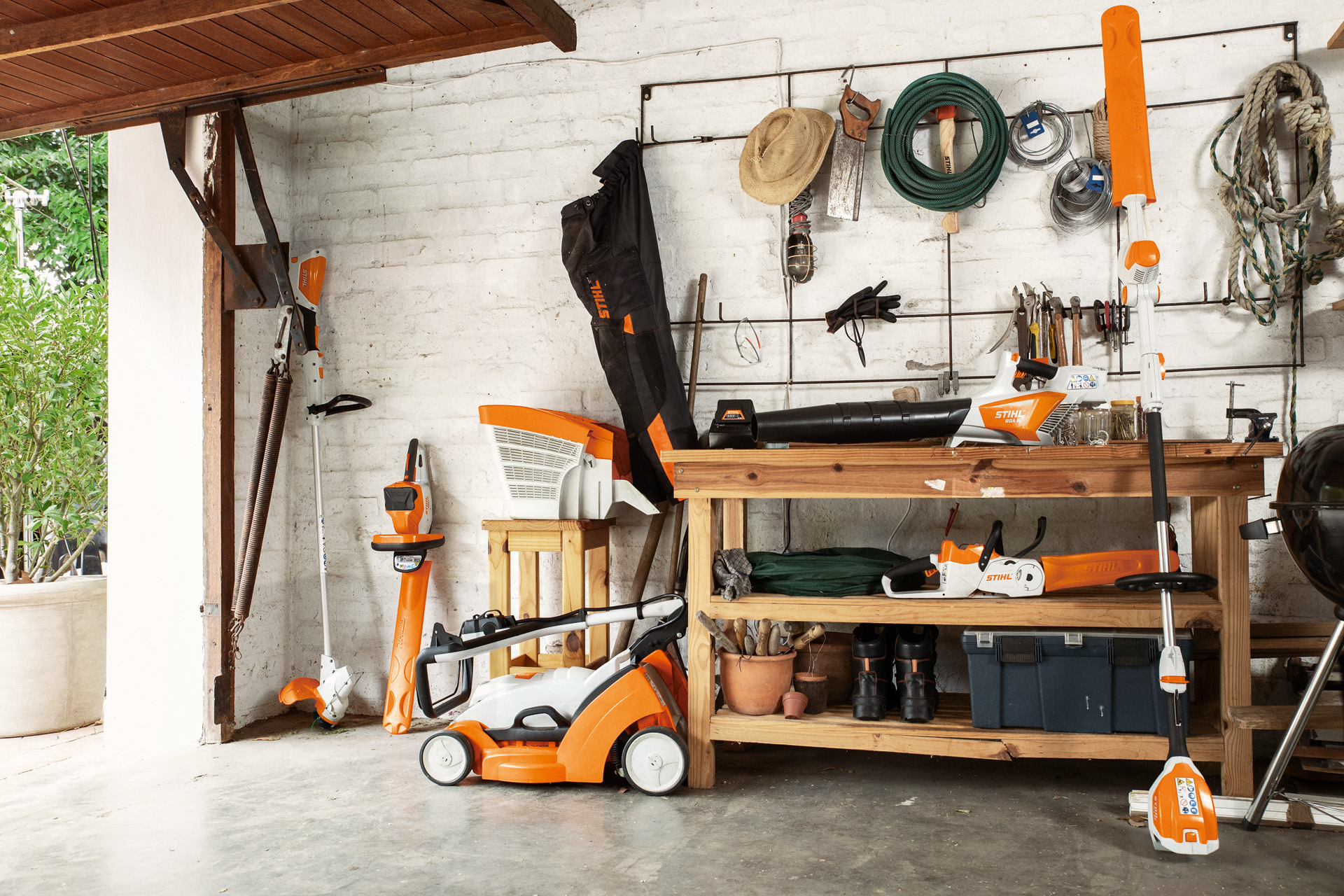 Intérieur d’un garage avec un coupe-bordure STIHL FSA 56 à batterie et un taille-haie STIHL HSA 56 à batterie posés contre le mur, et une tondeuse RMA 339 à batterie juste à côté