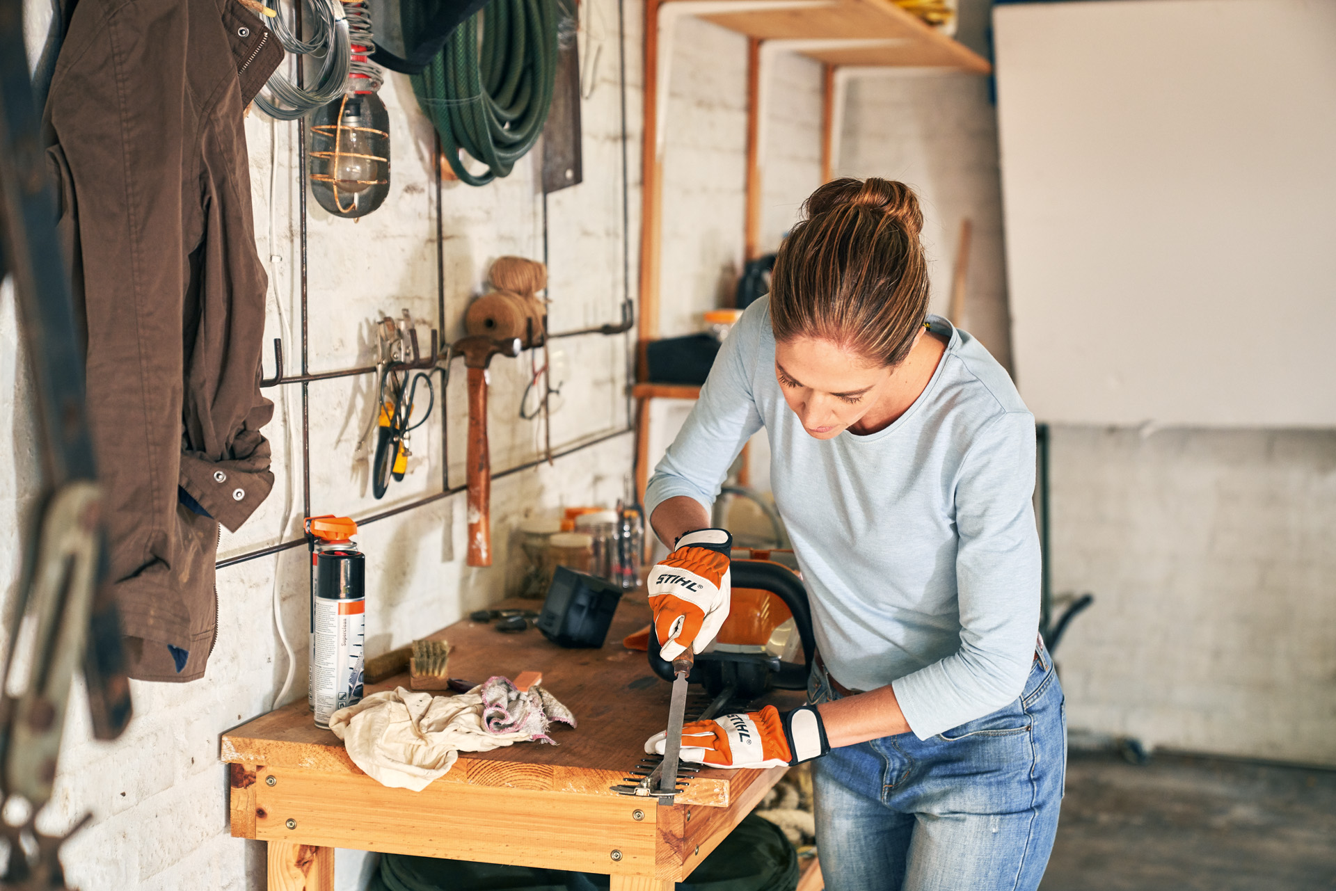 Une femme équipée des gants de protection, utilisant une lime plate pour affûter un taille-haie sur un établi en bois