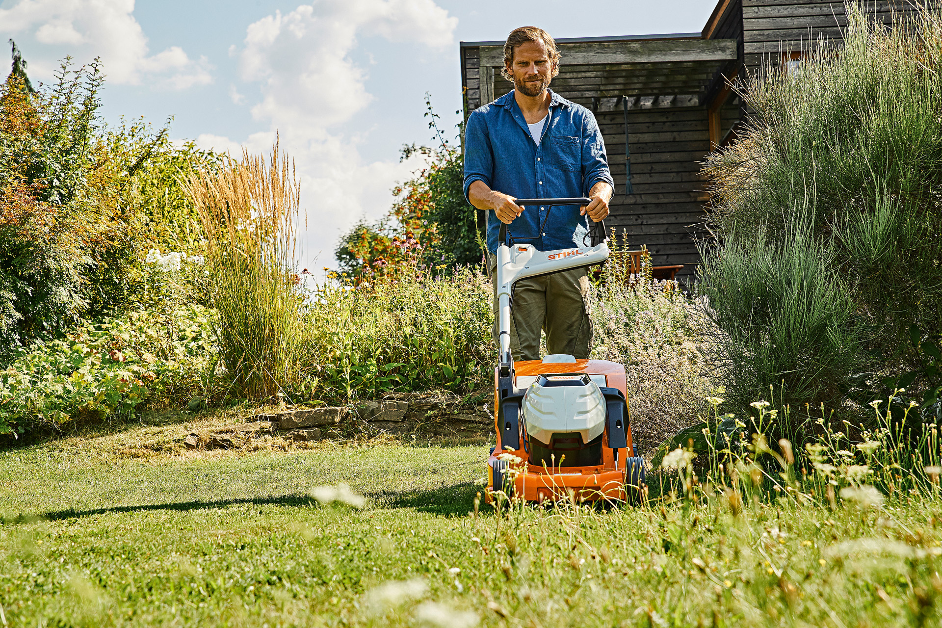 Un homme tond une pelouse à l’herbe haute avec une tondeuse à batterie STIHL RMA 448 TC, dans un jardin