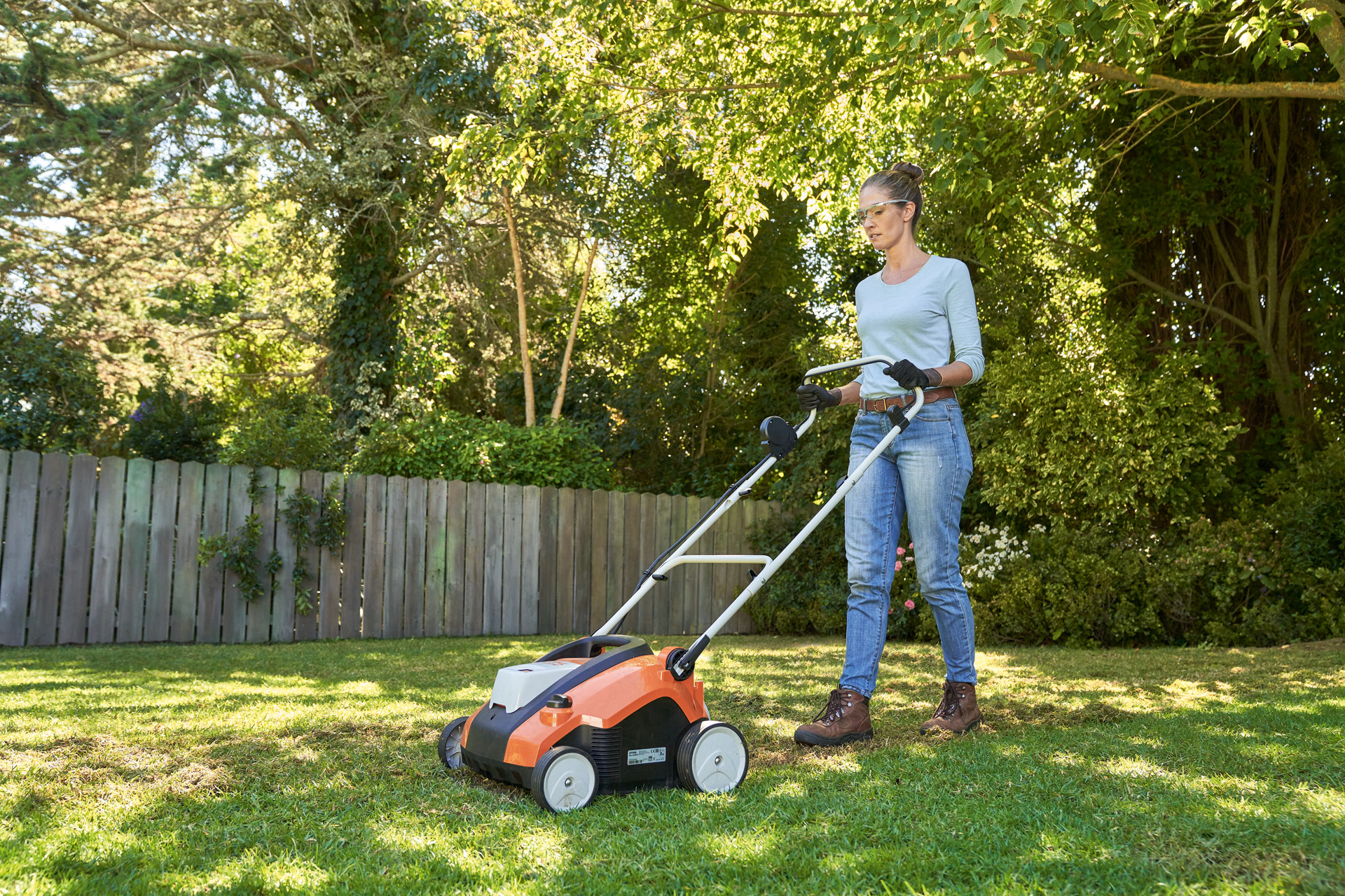 Une femme aère le gazon avec le scarificateur sur batterie STIHL RLA 240 dans un jardin, équipée de protections