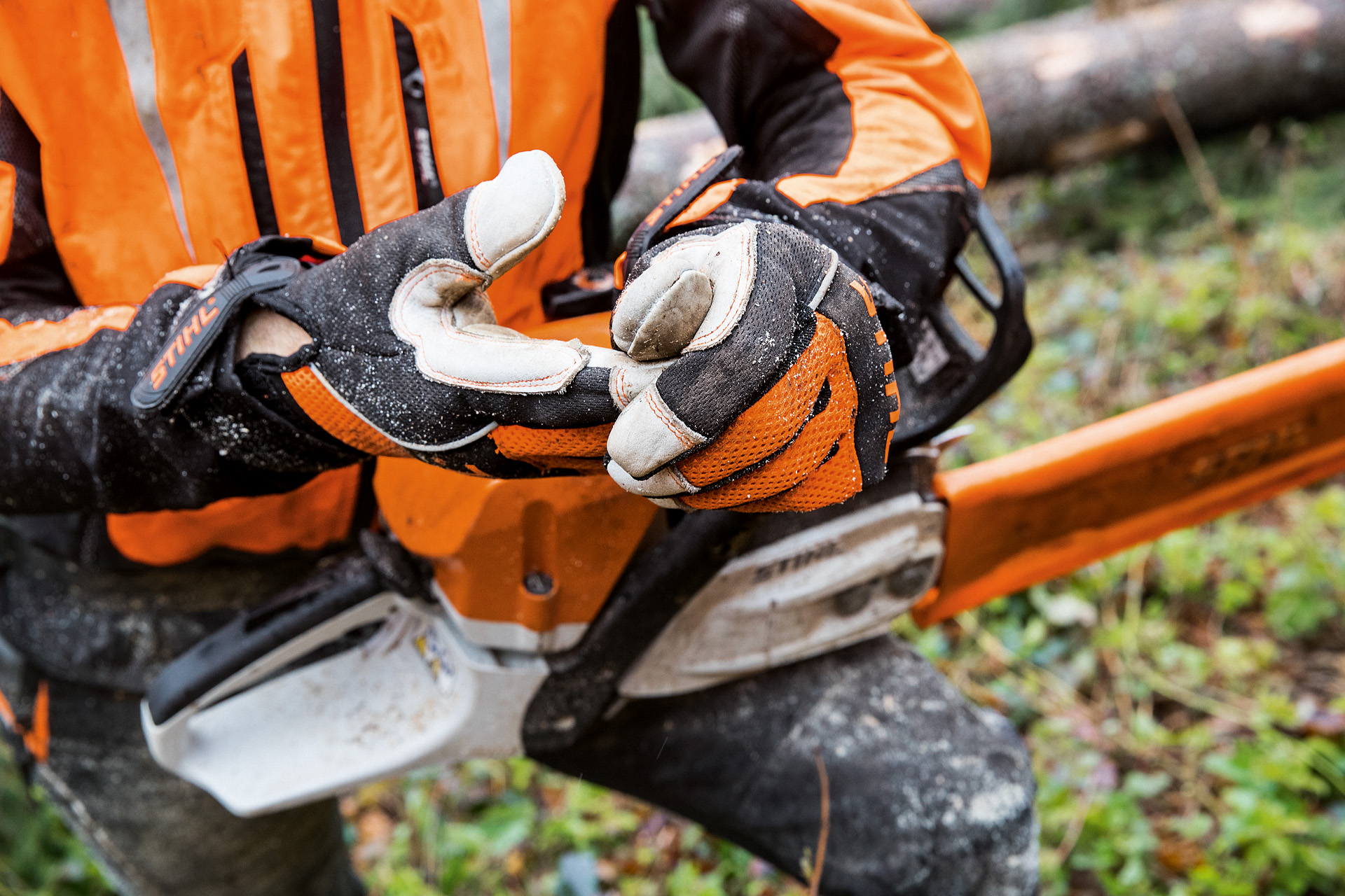 Gros plan sur les gants de protection anti coupure STIHL ADVANCE Ergo MS adaptés au travail à la tronçonneuse, portés par une personne tenant une tronçonneuse