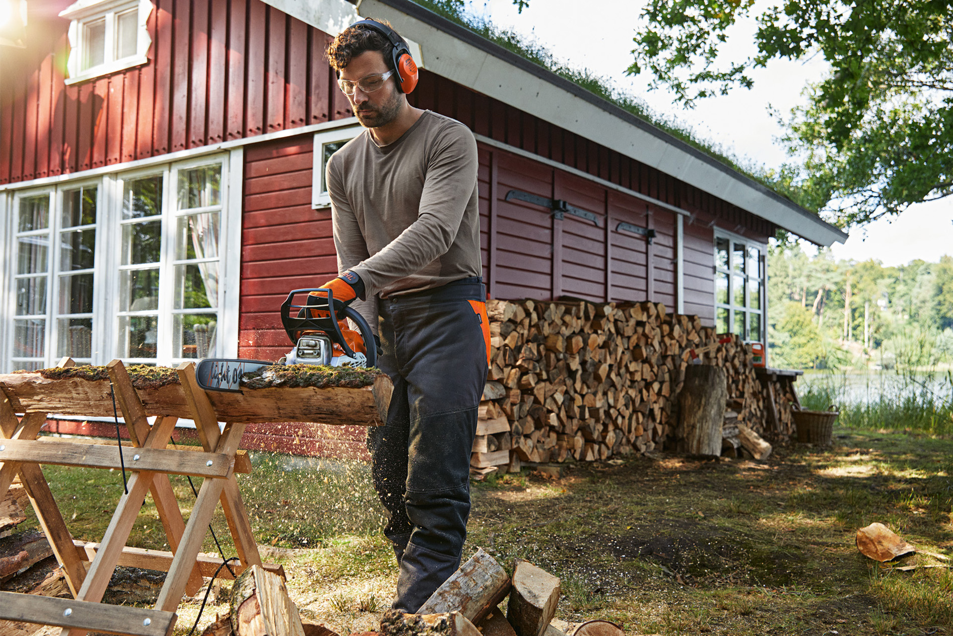 Un homme portant une protection auditive, coupe du bois de chauffage dans son jardin avec une tronçonneuse STIHL.