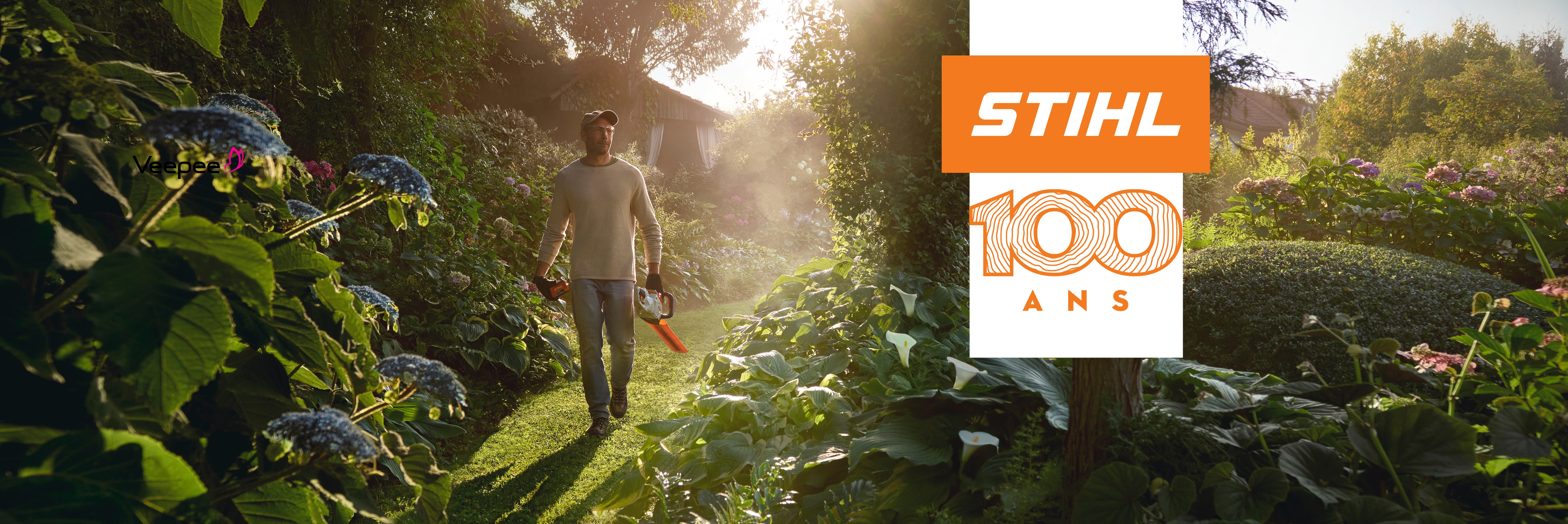 Un home marche dans son jardin avec un taille haie à batterie HSA 50 à la main et les rayons du soleil dans le dos