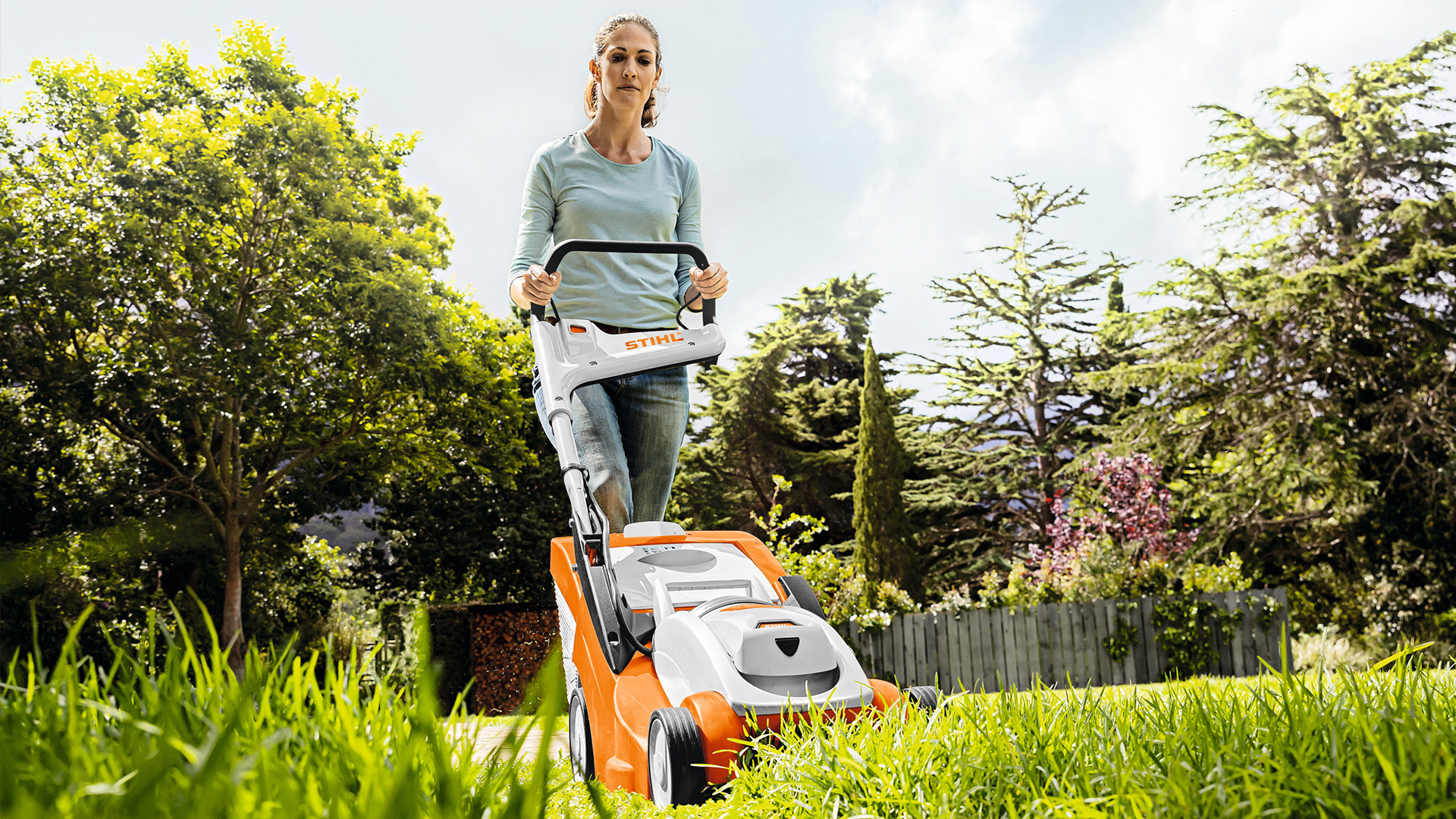 Une femme qui tond la pelouse avec une tondeuse à gazon à batterie STIHL