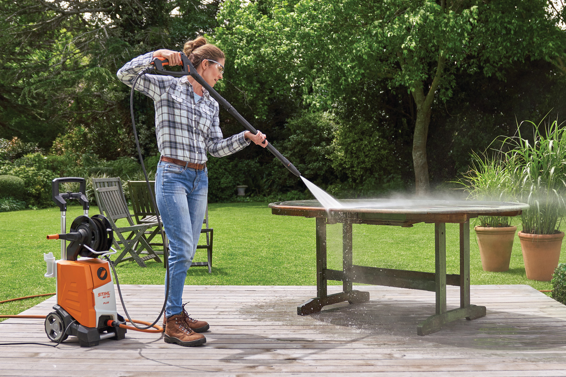 Une femme qui utilise un nettoyeur haute pression STIHL RE 130 PLUS pour nettoyer son mobilier de jardin