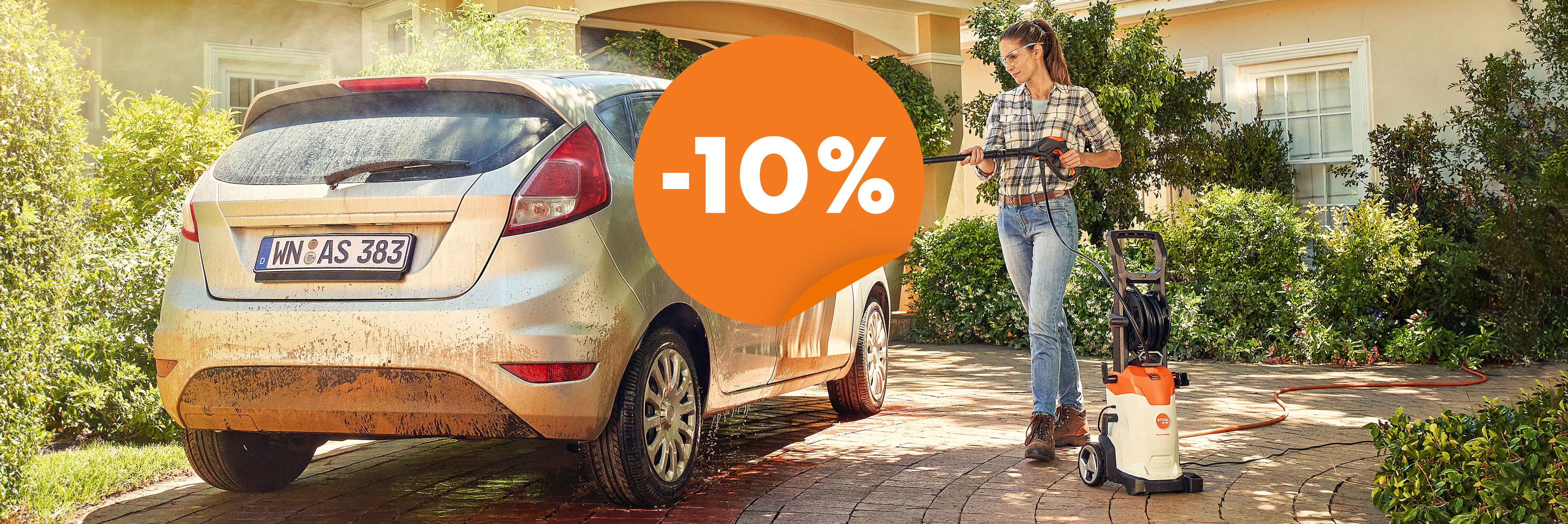 une femme nettoie sa voiture devant sa maison à l'aide d'un nettoyeur haute pression STIHL