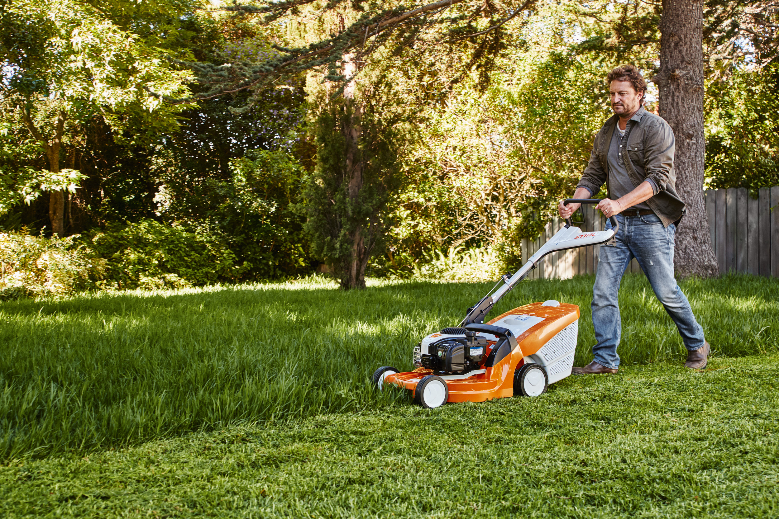 Un homme tond la pelouse dans un jardin avec une tondeuse à gazon STIHL 