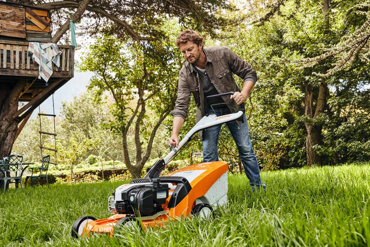 Homme en train de tondre une pelouse avec une tondeuse thermique STIHL RM 448 TC