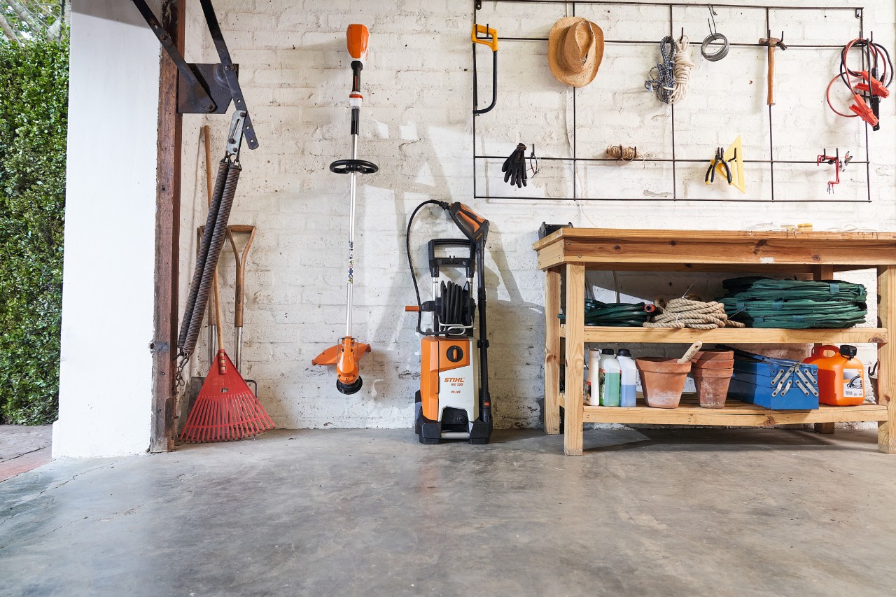 Le nettoyeur haute pression STIHL RE 130 plus et une débroussailleuse STIHL entreposés avec des outils de jardin dans un garage