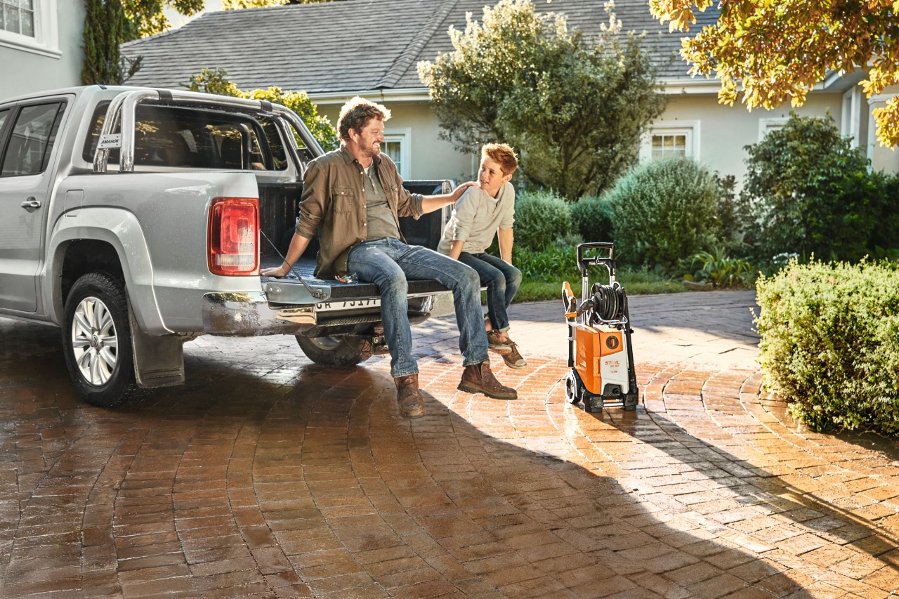 Un père et son fils assis à l’arrière d’un pick-up, nettoyeur haute pression STIHL RE 130 plus à côté du véhicule.