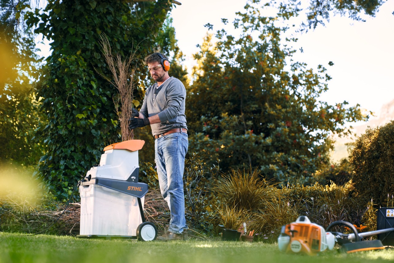 Homme avec broyeur à essence STIHL entre des arbres et des arbustes devant une maison