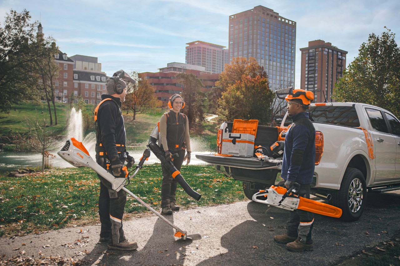 Un groupe de paysagistes professionnels, rassemblés autour de leurs véhicules, se préparent à travailler avec des outils à batterie STIHL.